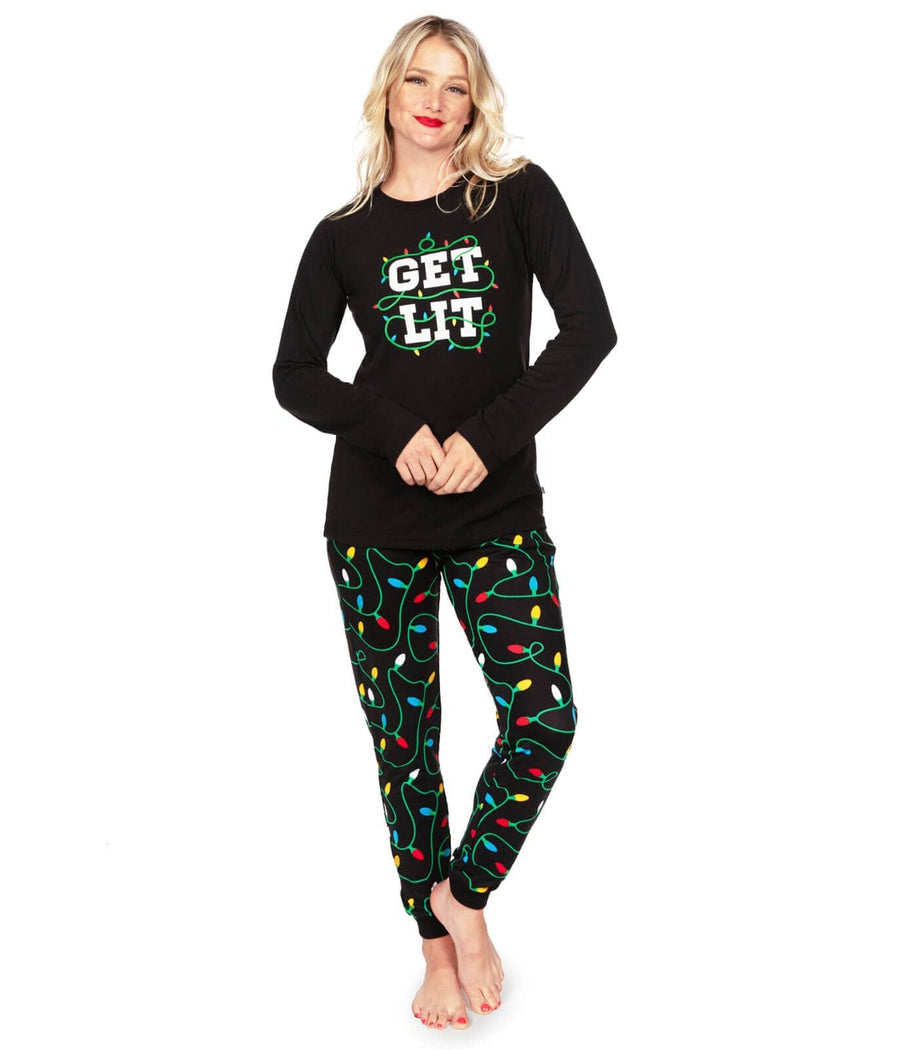 Woman wearing a black long-sleeve top with 'GET LIT' text and colorful Christmas lights pajama pants on a white background.