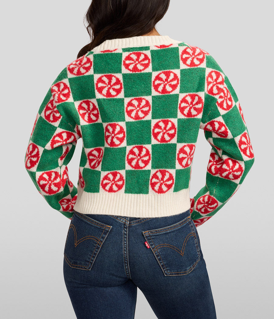 Person wearing a green and red checkered sweater with candy cane pattern on a plain background
